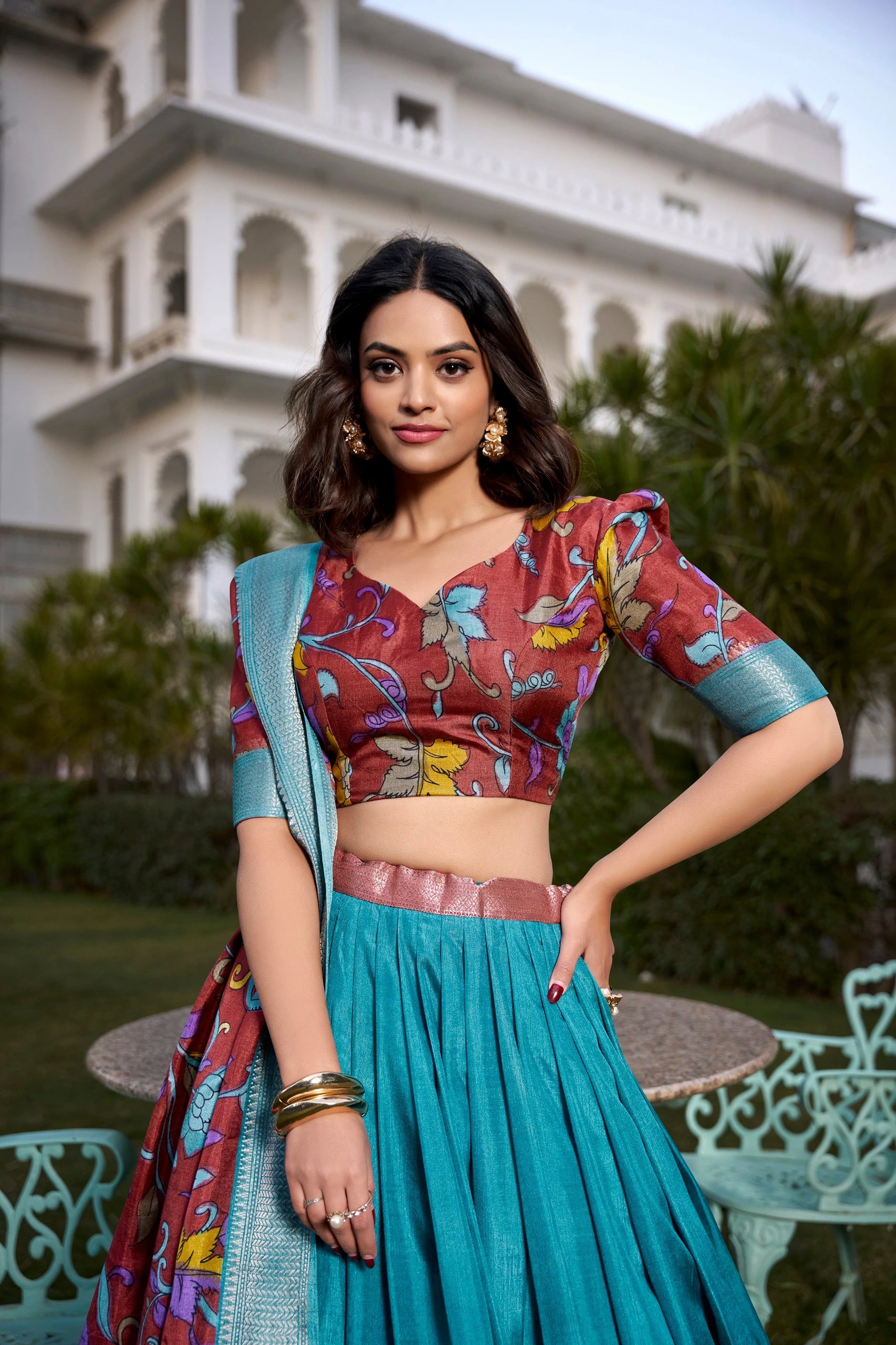 Woman in traditional outfit with colorful blouse and teal skirt in front of a building